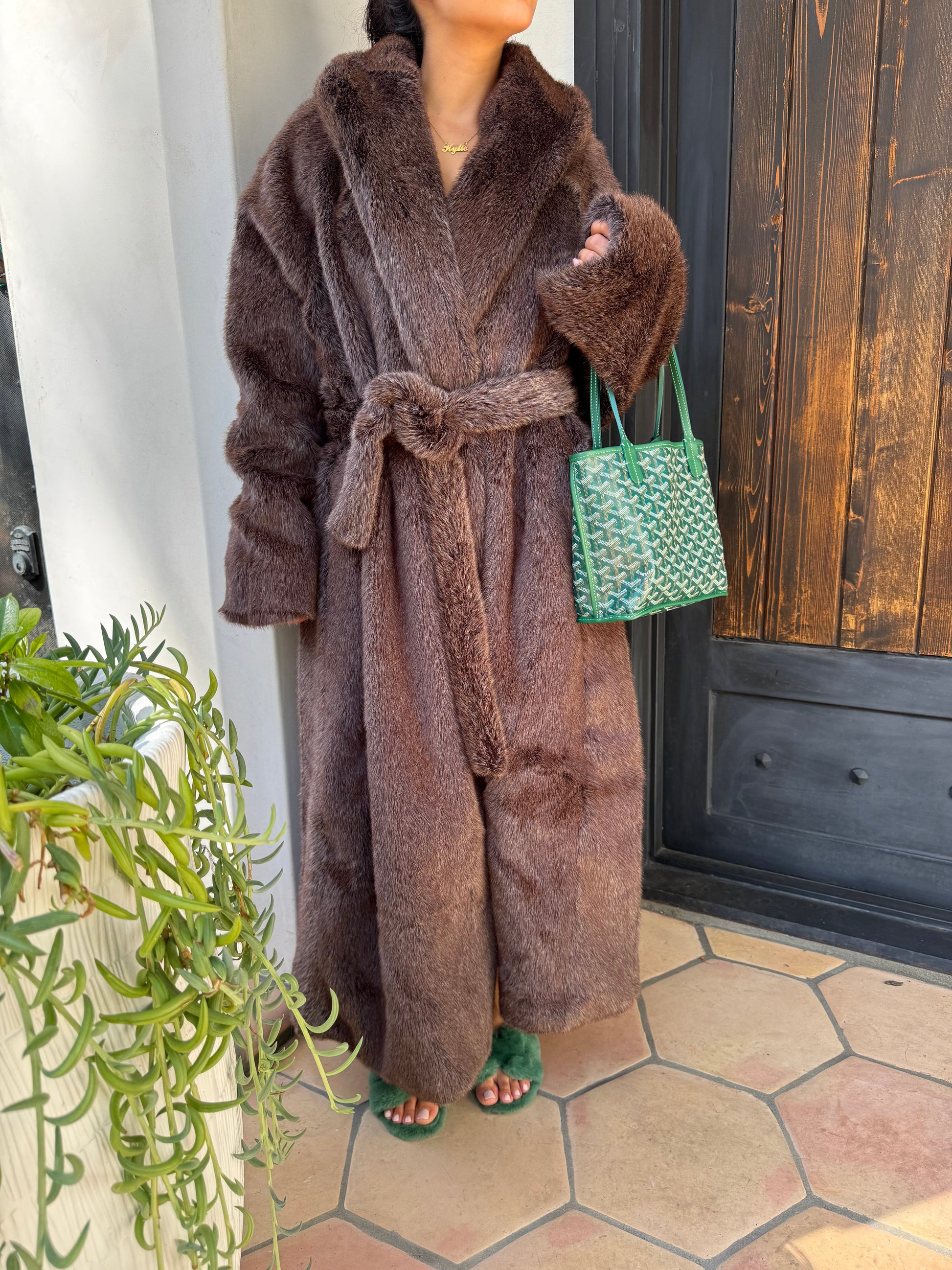 Brown robe with green accents on a white surface next to a plant