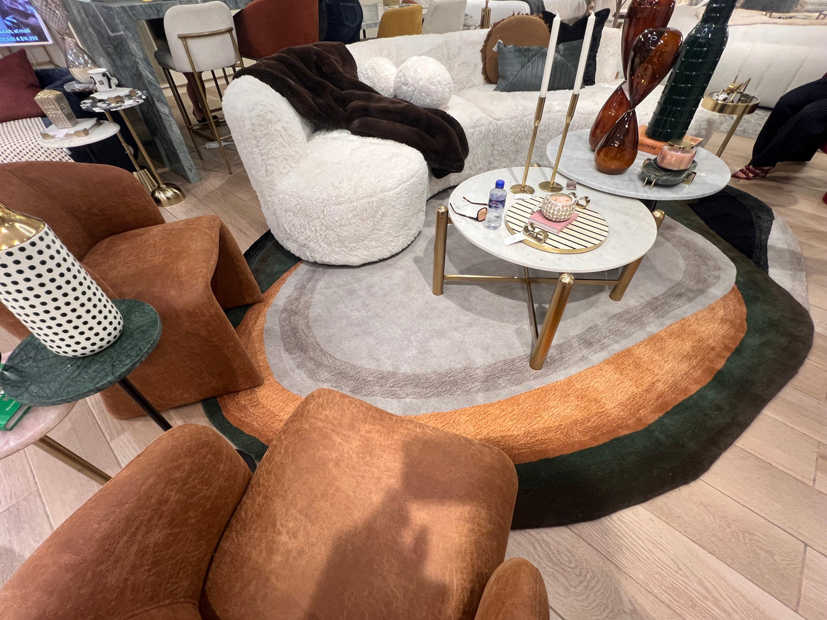 Modern living room with brown and white furniture, including a round ottoman and chairs.
