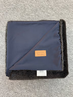 Folded navy blanket with black trim on a gray surface
