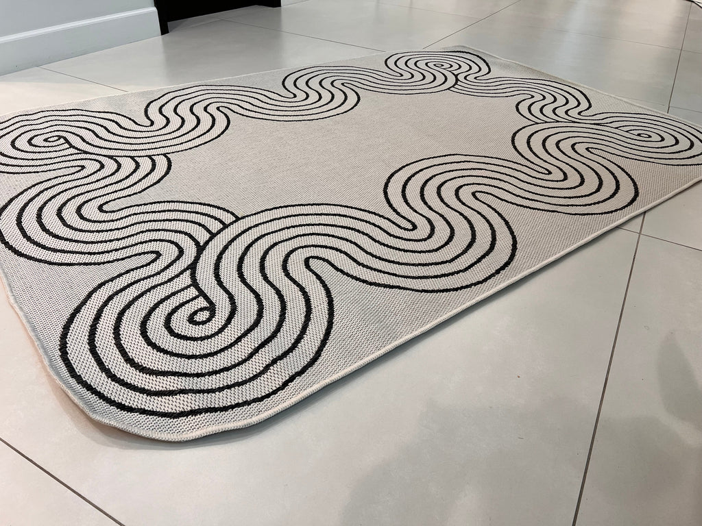 Indoor/Outdoor Ivory Rug with Black Geometric Swirl and Live Edge Design.