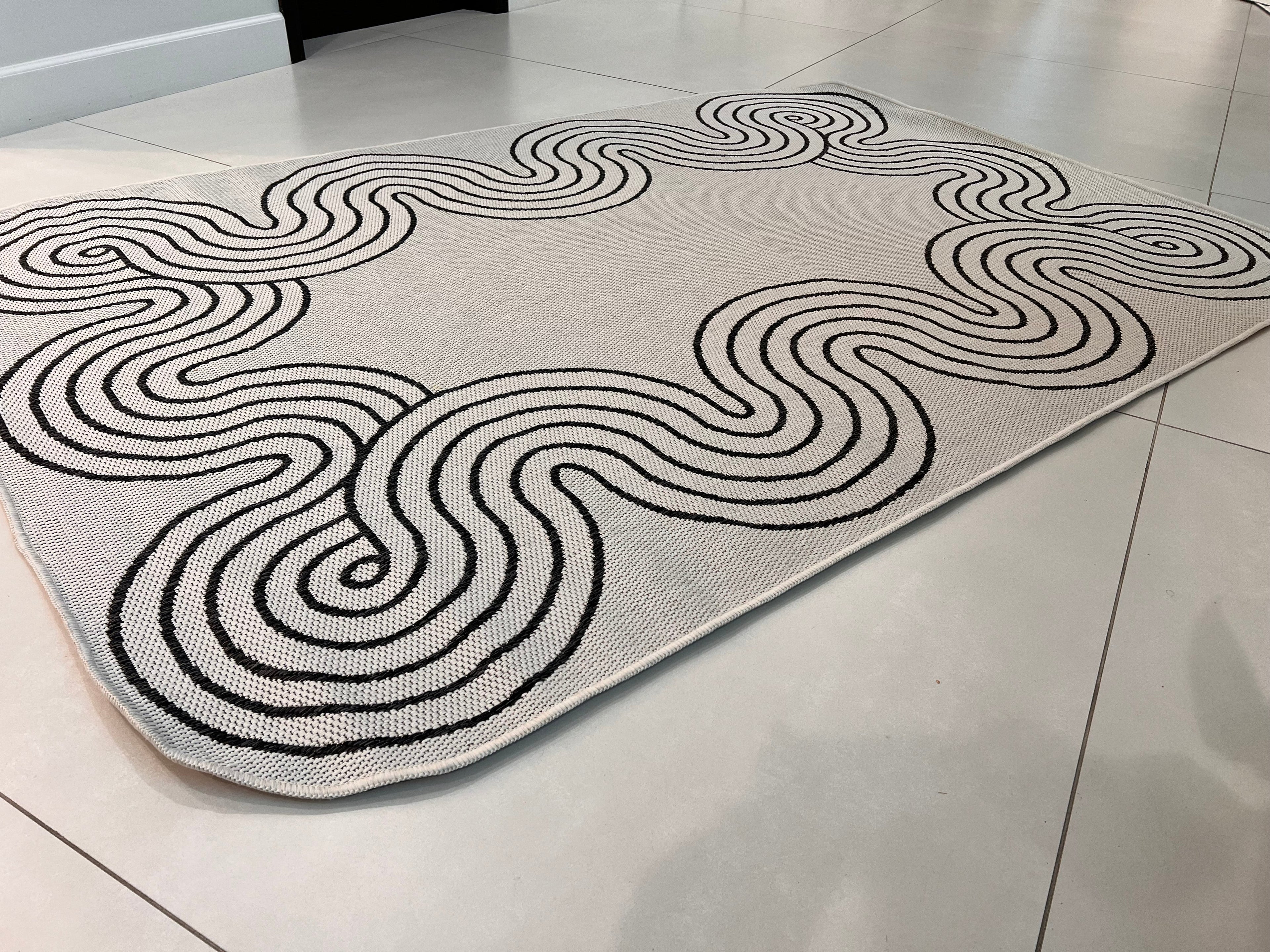 Indoor/Outdoor Ivory Rug with Black Geometric Swirl and Live Edge Design.