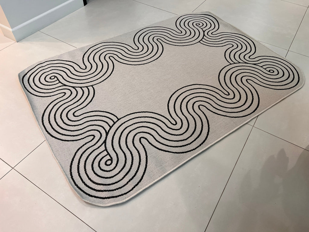 Indoor/Outdoor Ivory Rug with Black Geometric Swirl and Live Edge Design.