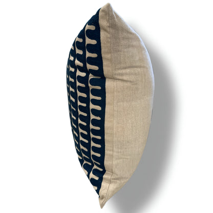A square decorative throw pillow shown in profile against a white background. The pillow features a split design: one half is a solid beige linen fabric, and the other half has a navy blue background with a repeating beige wavy geometric pattern.