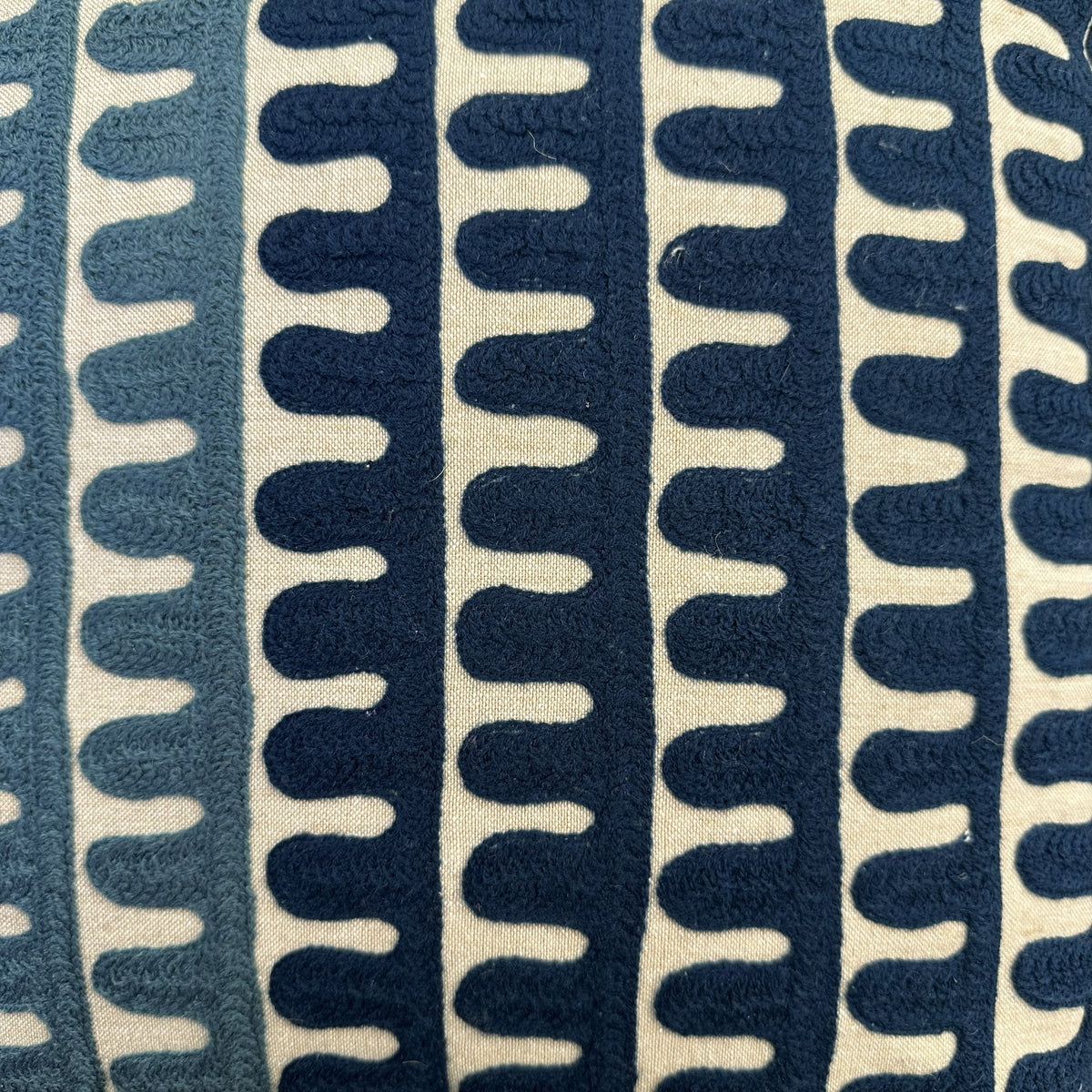 A close-up of a textured fabric with a repeating vertical wavy pattern in navy blue and cream.