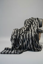 Gray textured throw blanket draped over a chair on a light gray background
