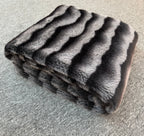 Folded fur blanket with a striped pattern on a textured surface