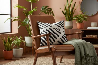 A mid-century modern brown leather armchair in a styled room setting, featuring a black and white striped throw pillow and a green knit throw blanket.